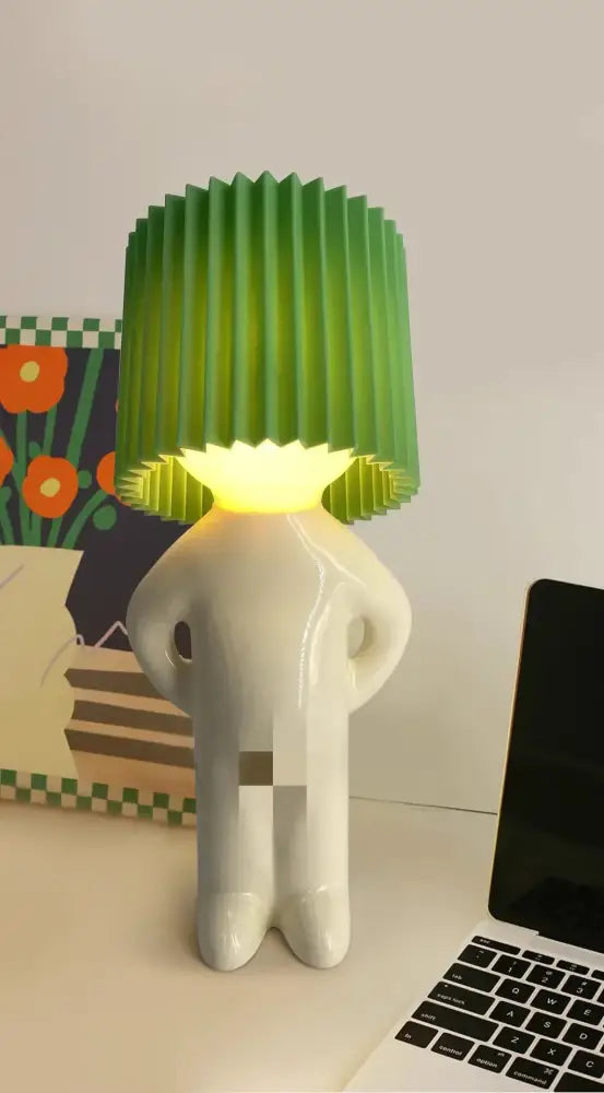 A white glossy figurine lamp with a green pleated shade providing warm light decorbites led pleats table lamp