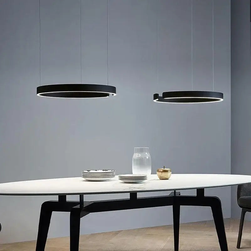 Two sleek black led ring chandeliers with illuminated edges hang above a modern dining room table by decorbites