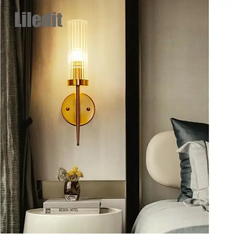 Gold-toned metal decorbites led sconce with cylindrical glass shade and vertical ridges for bedroom and home use