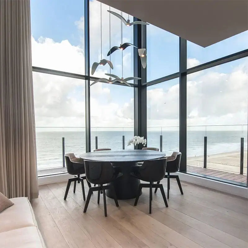 Black round dining table with sleek modern design and central pedestal base paired with decorbites led seagull chandelier