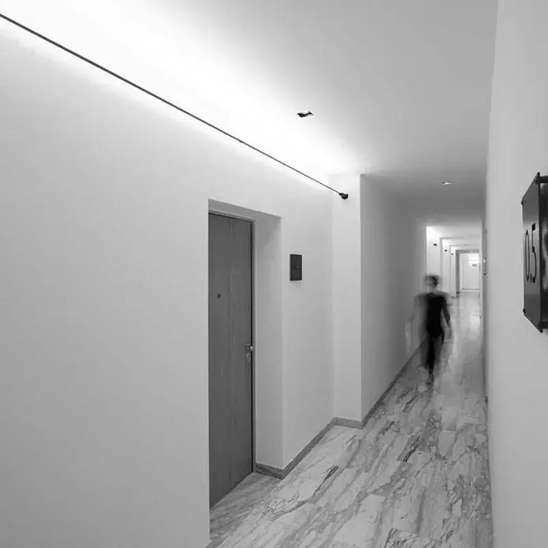 A hallway with white walls and marble flooring illuminated by decorbites led skyline steel pendant lights