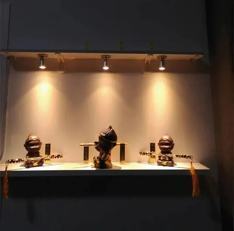 Three golden-brown monkey figurines with decorative tassels illuminated by decorbites led spotlight for cabinet display