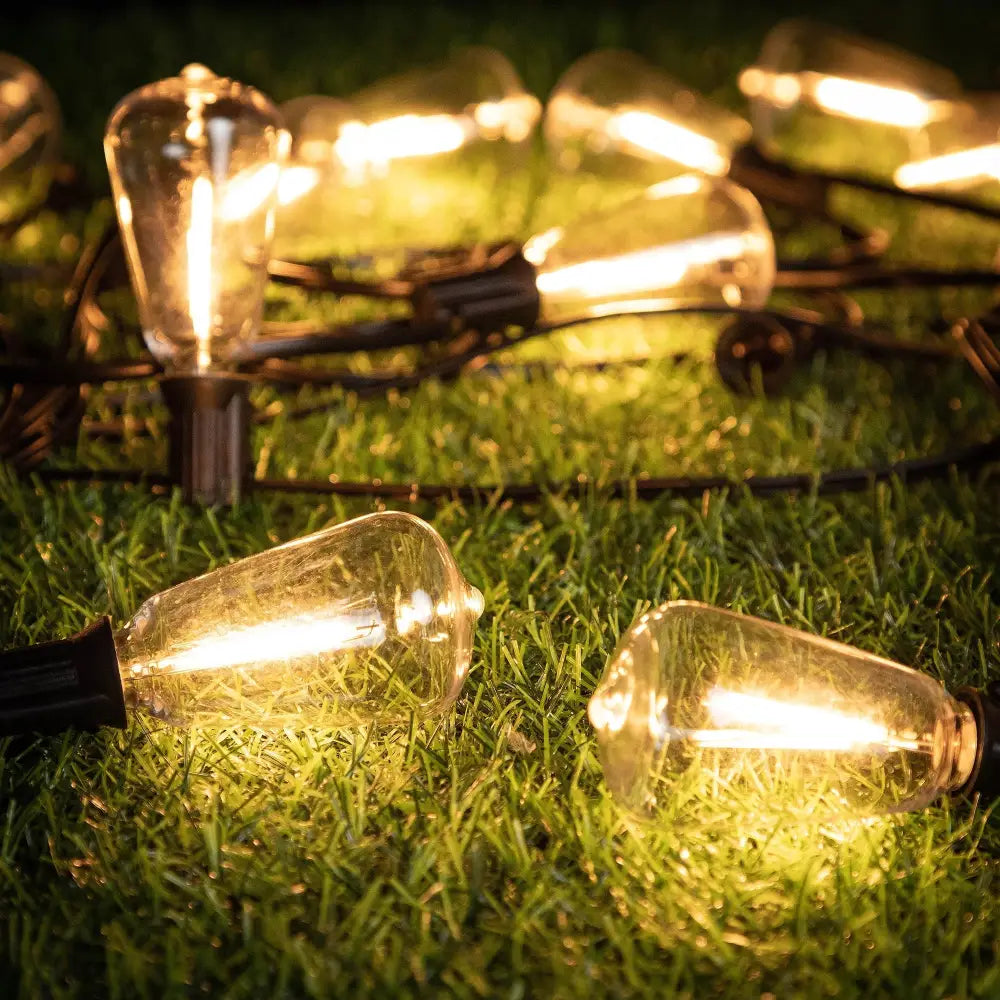 Warm glowing decorbites led string light bulbs with black bases lie on green grass for decorative use