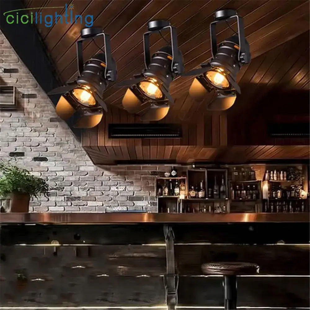 Three black decorbites led surface mount spotlights with warm amber glass shades hang from a wooden ceiling