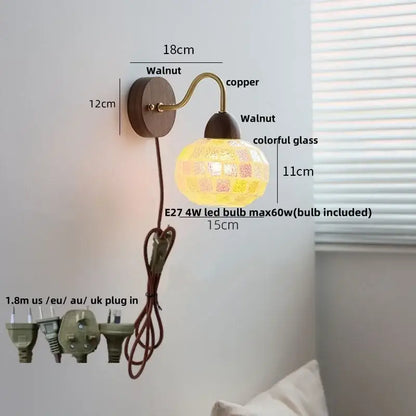 A warm glowing decorbites led tiffany style wall sconce with walnut wood base copper arm and colorful mosaic glass lampshade