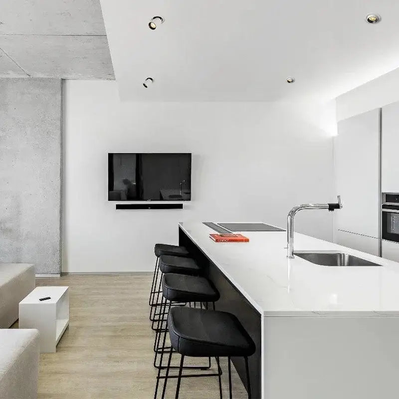 White marble kitchen island with stainless steel sink and black stools illuminated by decorbites led transformer downlight