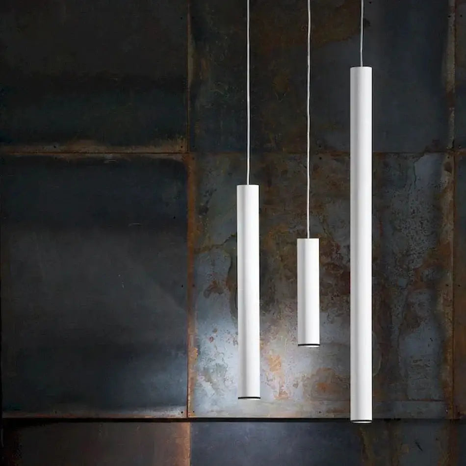 Three minimalist white cylindrical decorbites led tube pendant lights hang against a rustic metal wall for kitchen decor