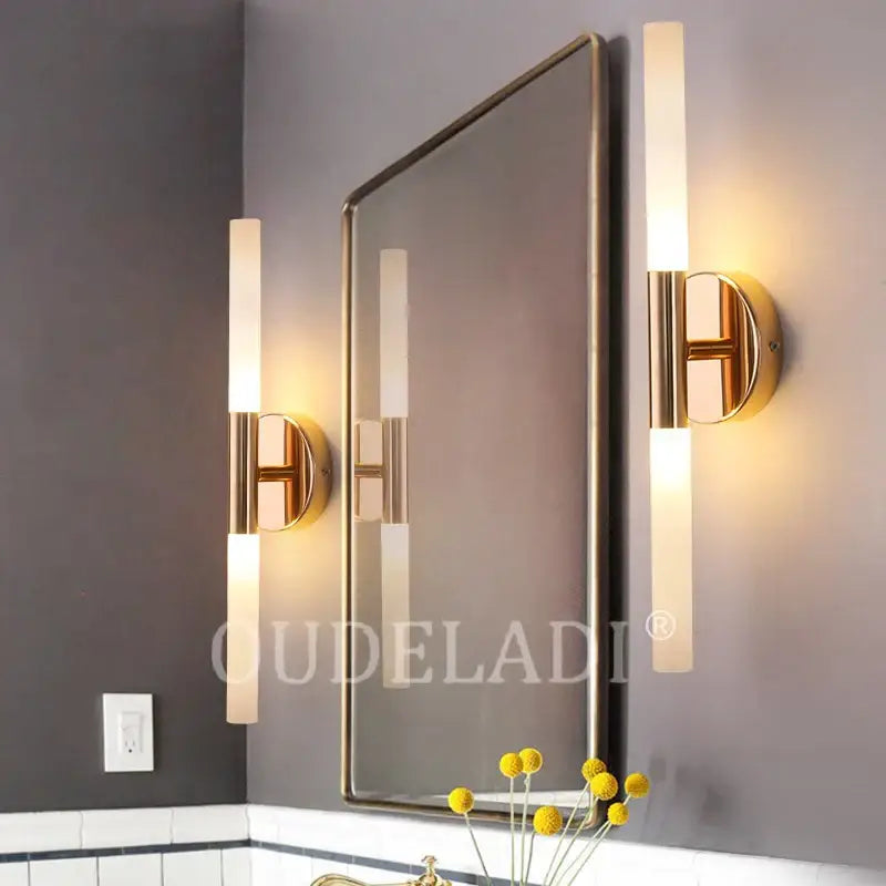Gold-finished decorbites led tube wall sconces with frosted glass tubes flank a rectangular mirror for modern interiors