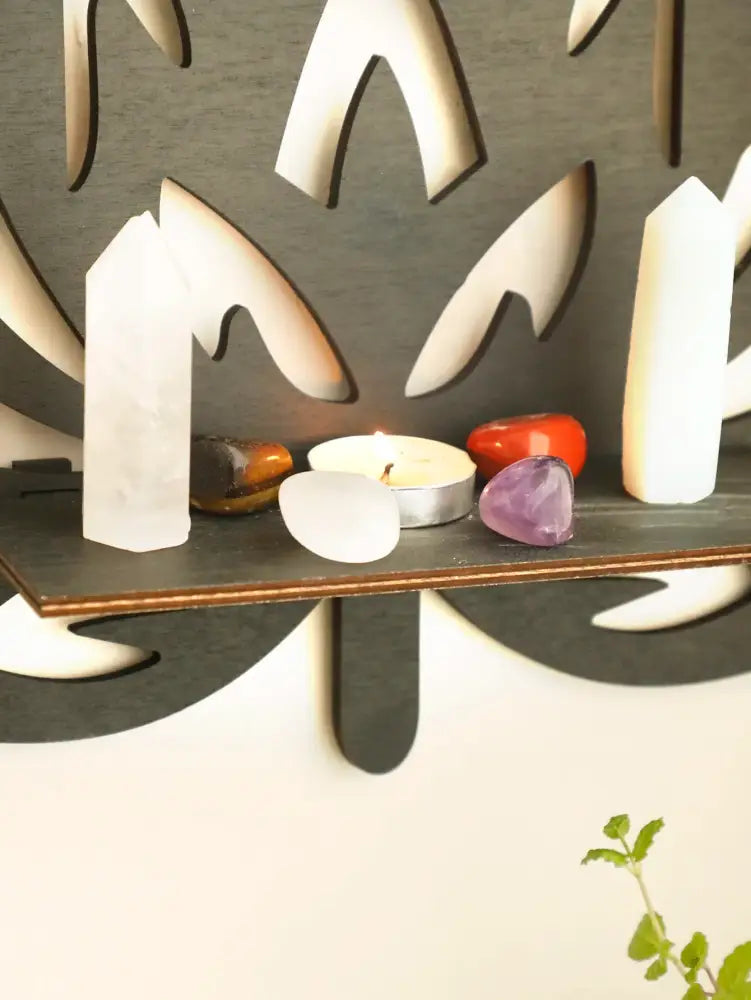 Dark gray wooden lotus floating wall shelf with tree-shaped cutout holding crystals and a lit tealight candle