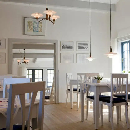 White wooden dining set with black cushioned seats under a decorbites lotus glass chandelier pendant light