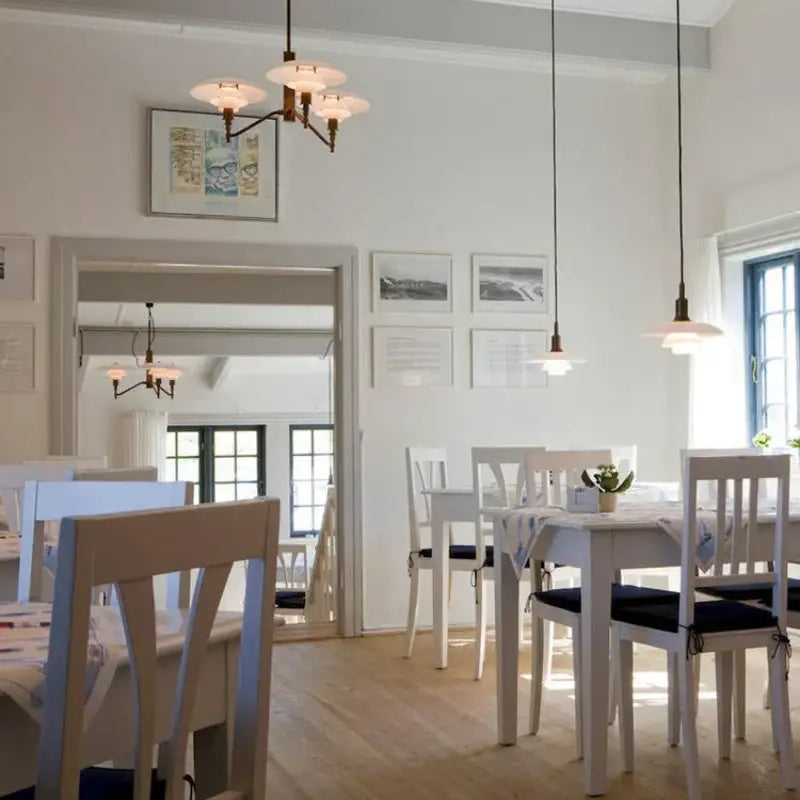 White wooden dining set with black cushioned seats under a decorbites lotus glass chandelier pendant light