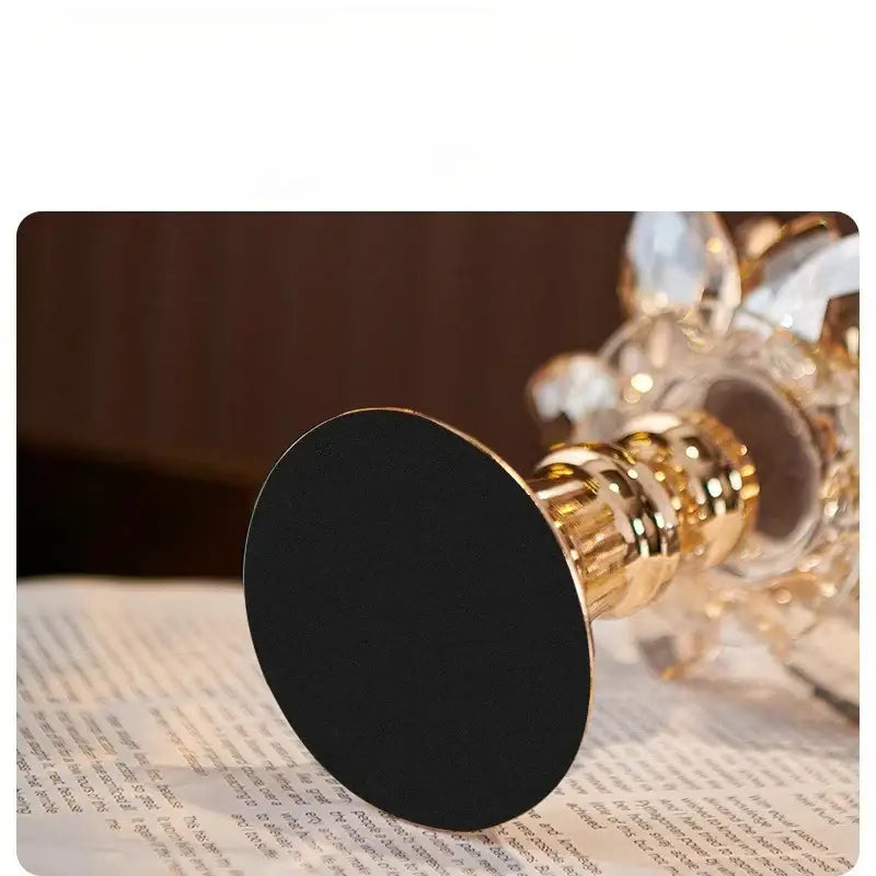 Gold-toned crystal candle holder with lotus glass flower design and black circular base for elegant home decor