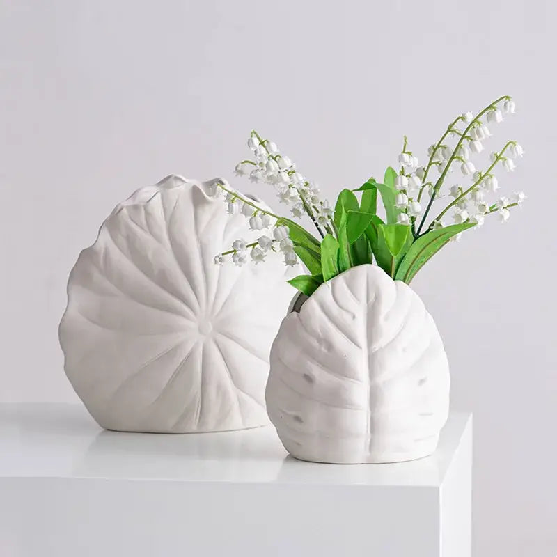 White ceramic decorbites lotus leaf vases shaped like leaves, one holding delicate white lily of the valley flowers