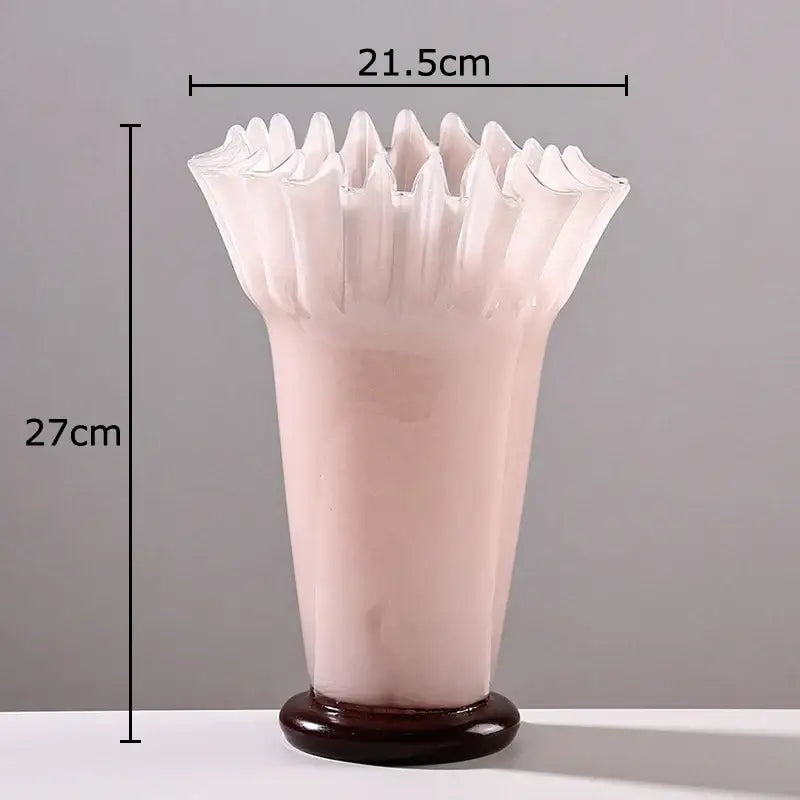 A translucent pink glass vase with a lotus leaf edge rim and dark brown wooden base for table flower decor