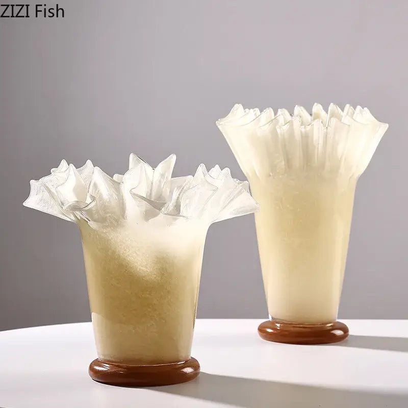 Two translucent cream-colored glass vases with lotus leaf edge ruffled tops and brown wooden bases for room decor