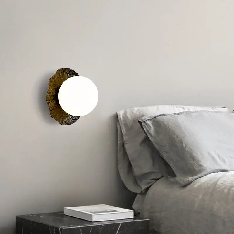 A modern wall lamp with a white glass shade and ornate bronze decorbites lotus leaf led base for Nordic living room