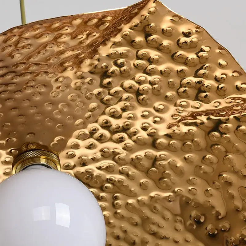 Gold-toned hammered metal pendant light with textured bubbly surface and white bulb from decorbites lotus leaf pendant collection