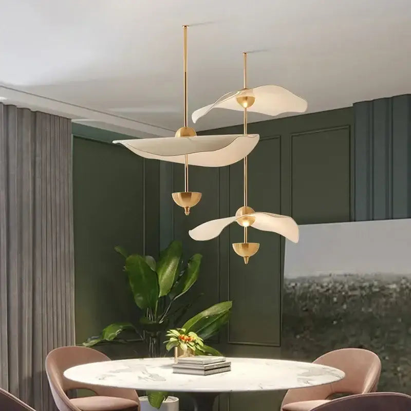 Gold-toned decorbites lotus leaf pendant lights with sculptural white petal shades hang above a dining table