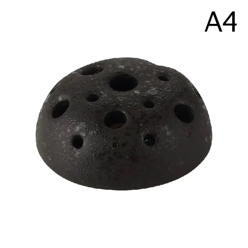 Black textured ceramic vase with multiple circular holes resembling lotus seedpod made from stone sand material