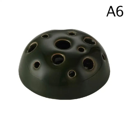 Dark green ceramic vase shaped like a lotus seedpod with multiple circular holes in stone sand texture design