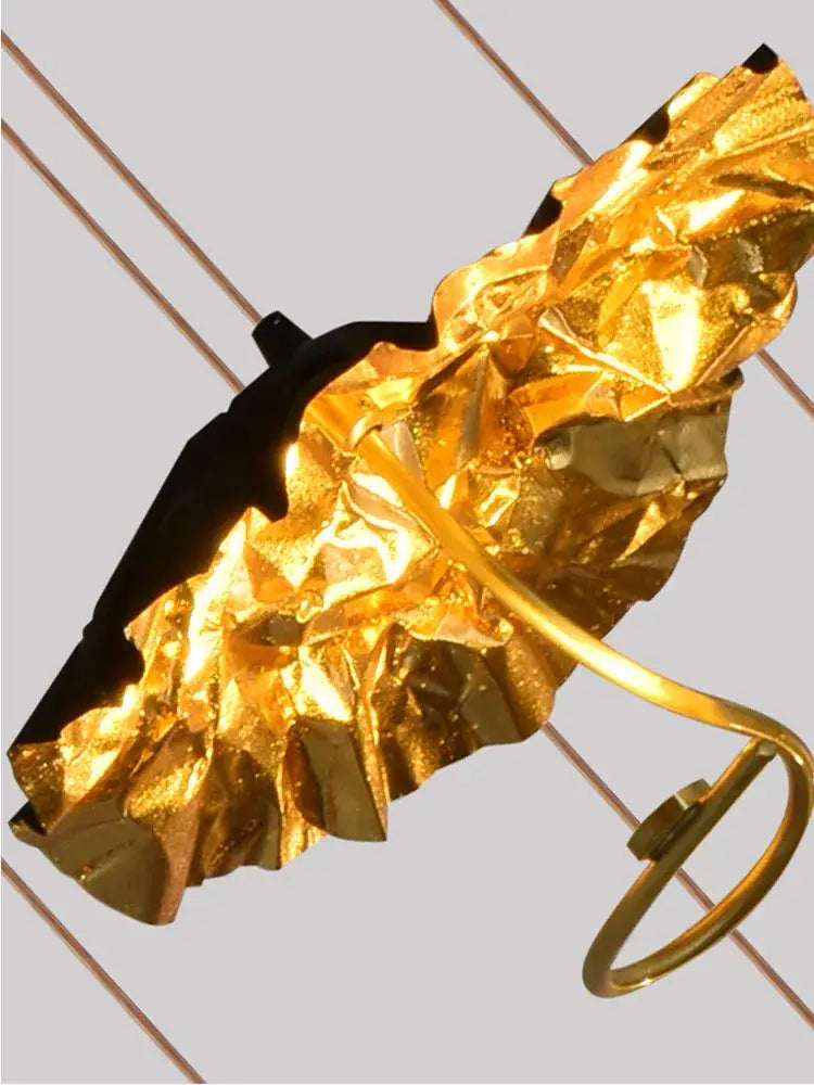 A crinkled gold foil umbrella with a black handle and golden metal frame in decorbites lotus staircase chandelier