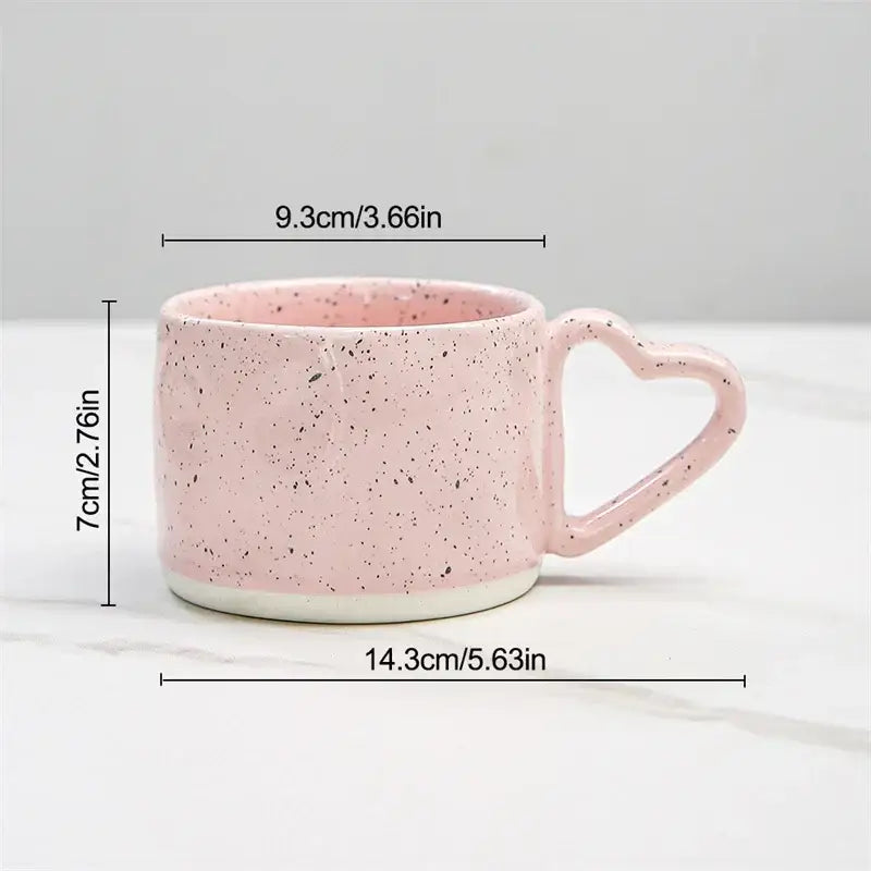 A pink speckled decorbites love handle ceramic cup with heart-shaped handle and white base for breakfast tea or coffee
