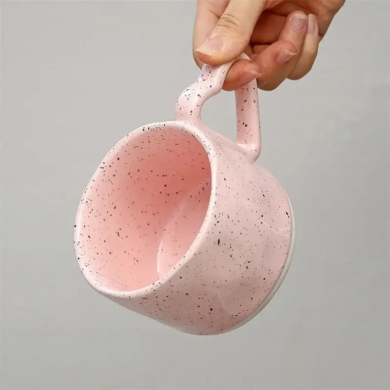 A pink speckled decorbites love handle ceramic cup held by hand ideal for breakfast tea coffee and office gifts