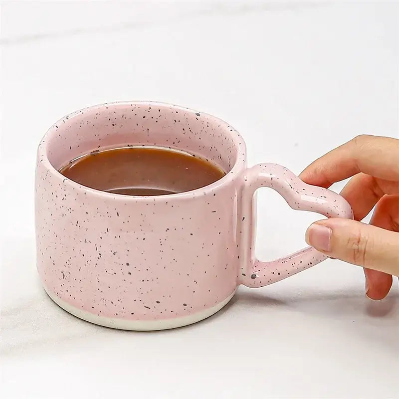 Pink speckled decorbites love handle ceramic cup with heart-shaped handle filled with dark tea or coffee