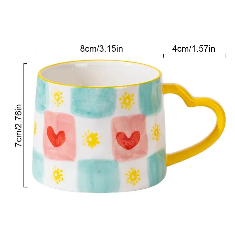 A decorbites love heart ceramic mug with a yellow heart handle and pink hearts and yellow suns on teal checkered background