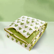 A neatly folded decorbites love print soft summer quilt with white and green hearts exterior and olive green interior with yellow piping