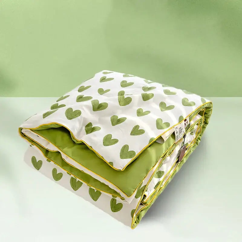A neatly folded decorbites love print soft summer quilt with white and green hearts exterior and olive green interior with yellow piping