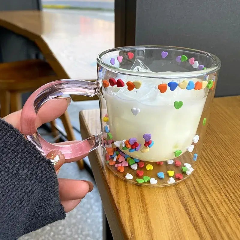 A clear glass cup with a pink handle featuring colorful heart sprinkles by decorbites love quicksand double bottom design