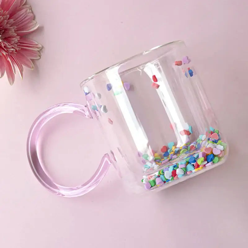 Clear glass cup with translucent pink handle and colorful heart confetti inside decorbites love quicksand double design