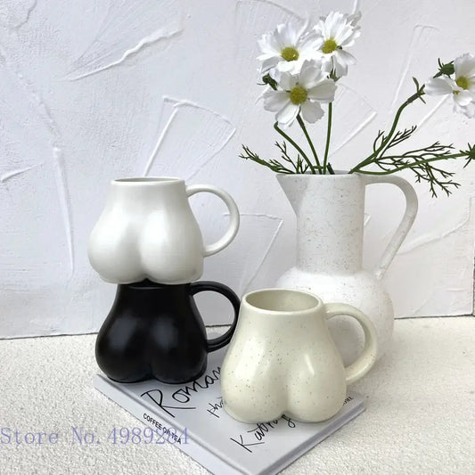 White ceramic coffee cup with playful sculpted buttocks shape and subtle speckled texture by DecorBites