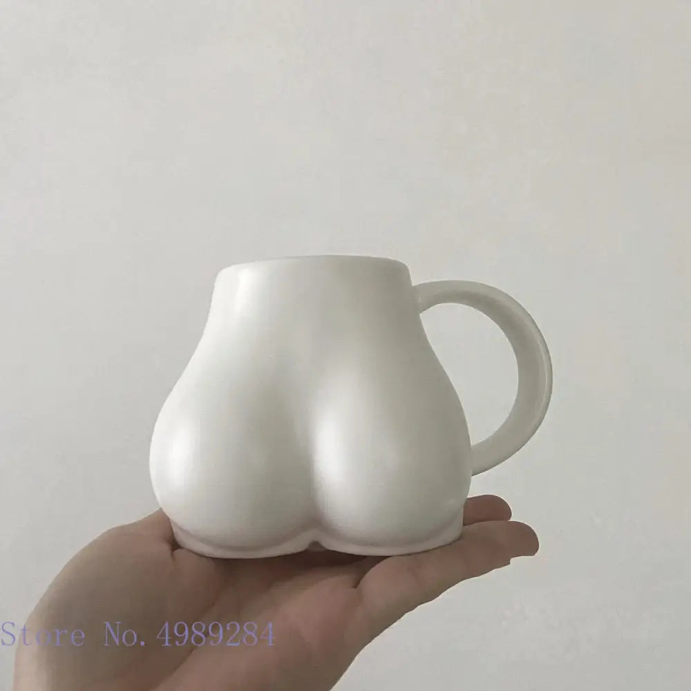 White ceramic coffee cup shaped like buttocks with smooth glossy finish and curved handle by decorbites