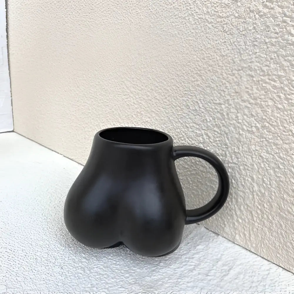 Black ceramic coffee cup shaped like buttocks with smooth glossy finish and curved handle by DecorBites™