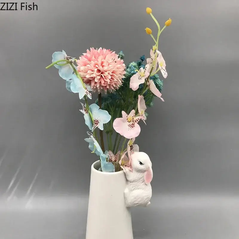 A white ceramic vase with a decorbites lovely rabbit figurine holding pastel pink and blue artificial flowers