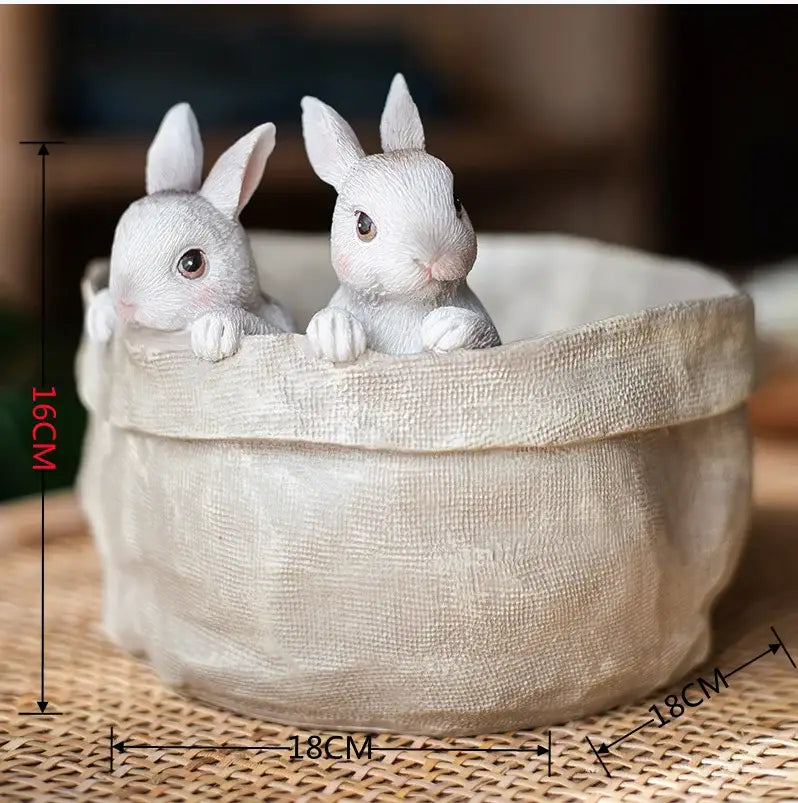 Two white resin bunny figurines peeking over a beige linen-textured decorbites lovely rabbit garden flowerpot