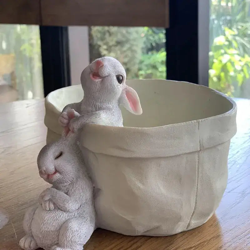 White resin lovely rabbit garden figurine with pink ears sitting beside beige fabric-lined rabbit garden flowerpot