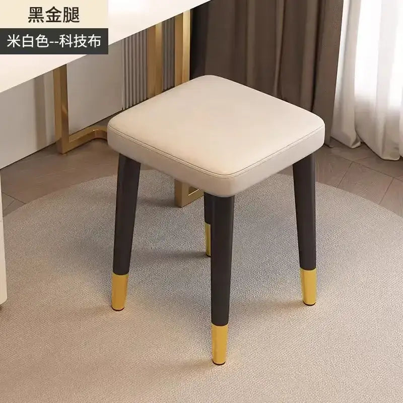 A decorbites low square stool bench with cream cushioned tech fabric seat and black legs with gold tips for dining use
