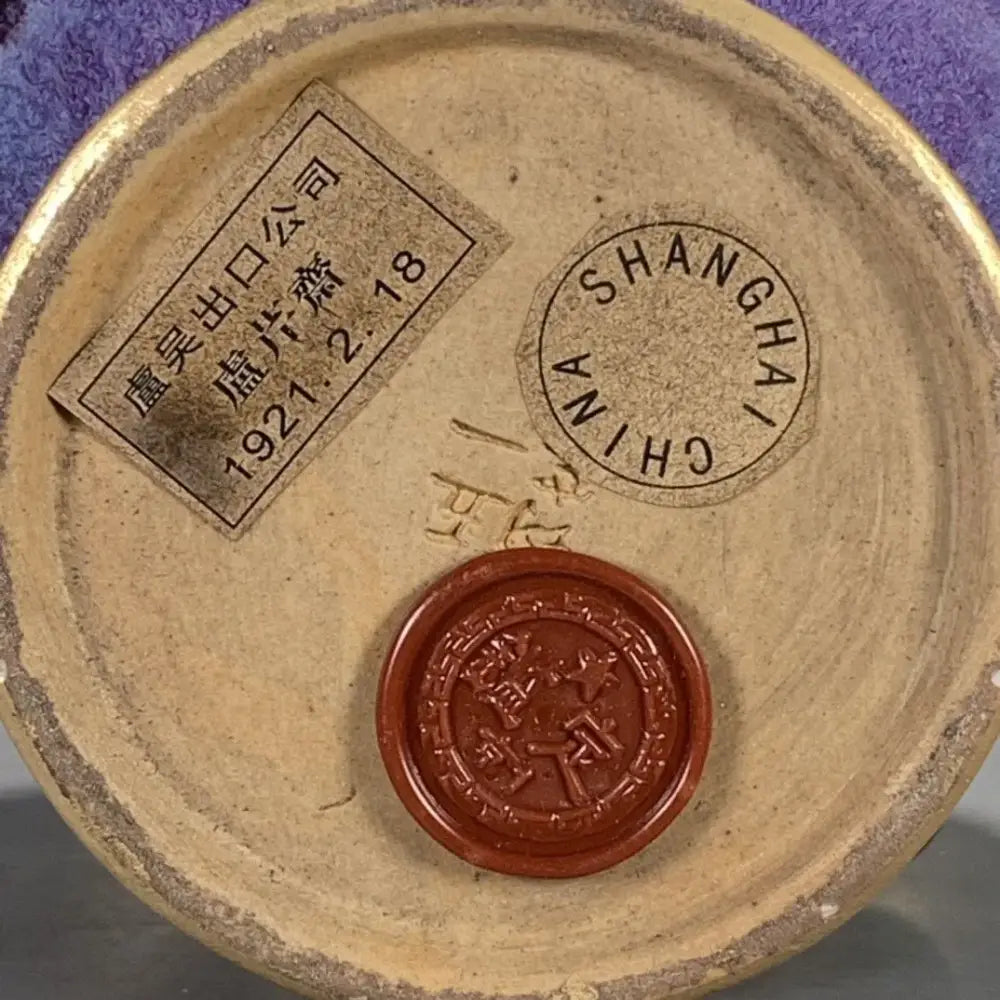 A brown circular ceramic seal stamp with embossed chinese characters on the base of a beige qinzhai jun porcelain bottle ornament by decorbites lu qinzhai