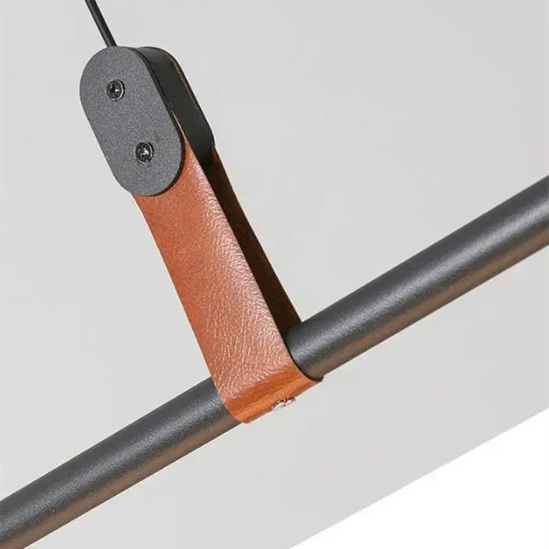 Brown leather strap with black metal hardware securing dark gray pipe in decorbites lucien tube chandelier pendant light fixture
