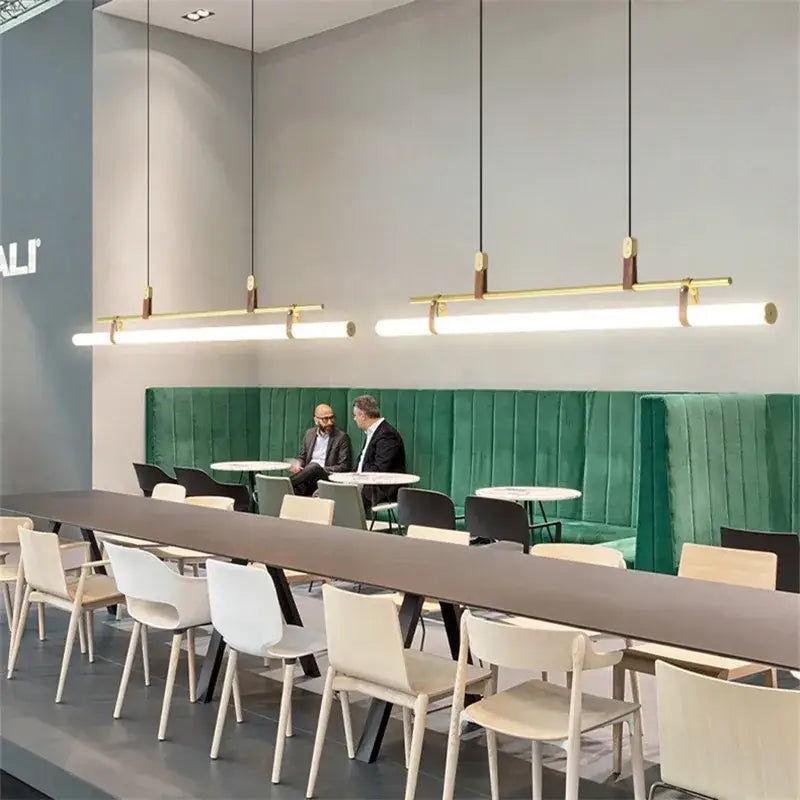 Modern gold-toned decorbites lucien tube chandelier with wooden accents hanging above a long café table