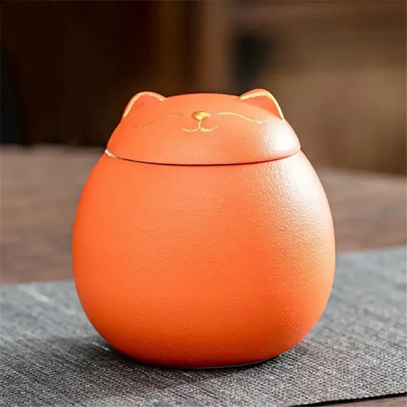 Orange ceramic tea storage jar shaped like a smiling cat with gold accents for household tea and candy storage