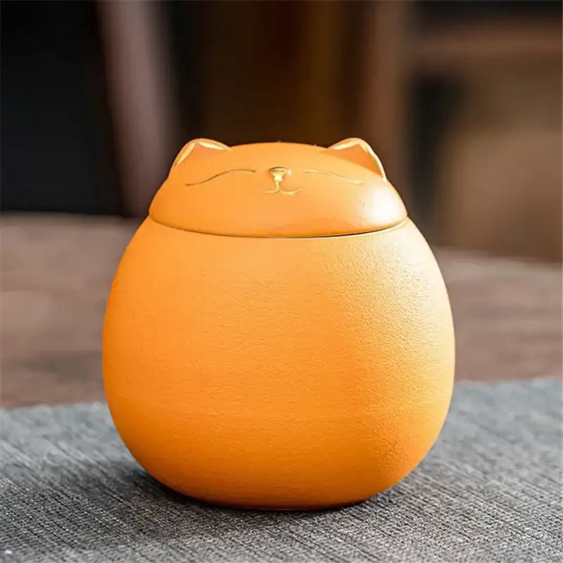 Orange ceramic cat-shaped tea storage jar with smooth rounded body and golden facial details for household use