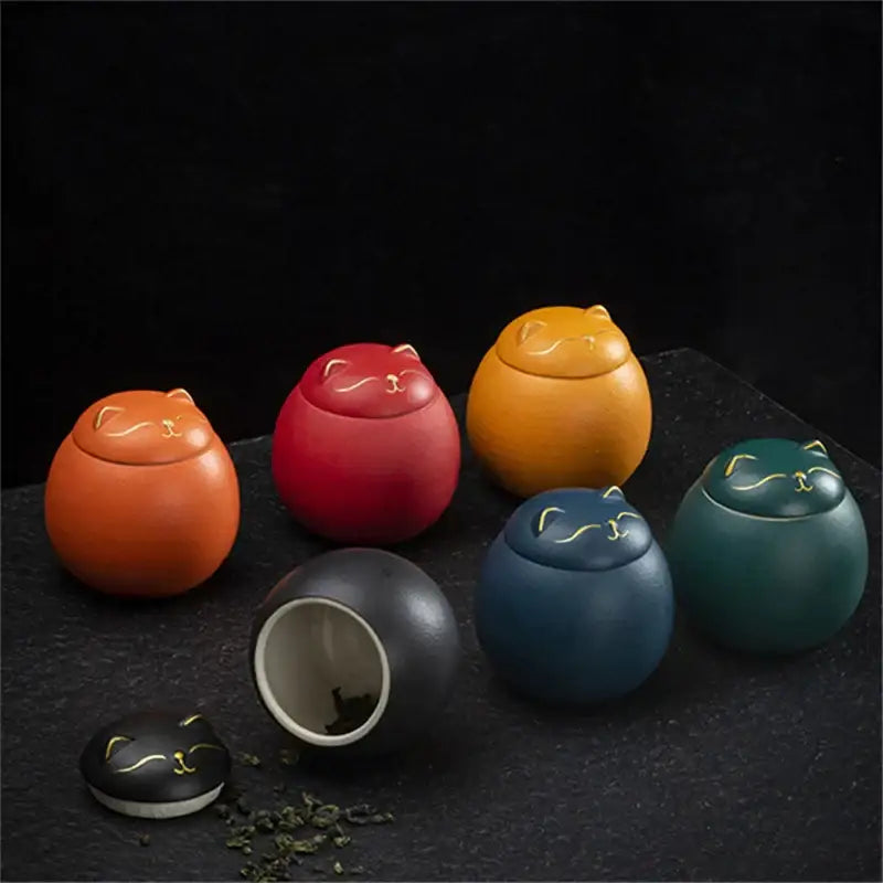 Collection of vibrant ceramic tea storage jars shaped like sleeping cats in orange red yellow blue and green colors