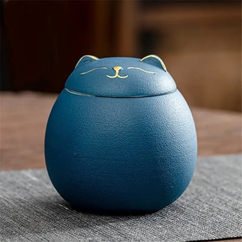A blue ceramic cat-shaped tea storage jar with gold-trimmed ears and a smiling face for household tea storage