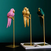 Three colorful resin ornament lucky parrot resin figurines in pink gold and teal on golden stands by decorbites lucky parrot