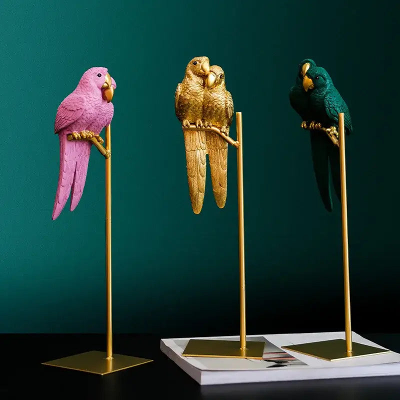 Three colorful resin ornament lucky parrot resin figurines in pink gold and teal on golden stands by decorbites lucky parrot