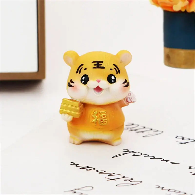 A cheerful yellow lucky tiger figurine holding golden bars in an orange outfit with chinese characters for new year decor